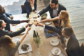 Coworkers in business attire toast glasses of wine at a corporate dinenr