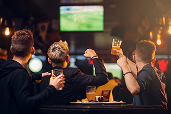 A group of men drink beer and watch a sporting event on a TV in a bar