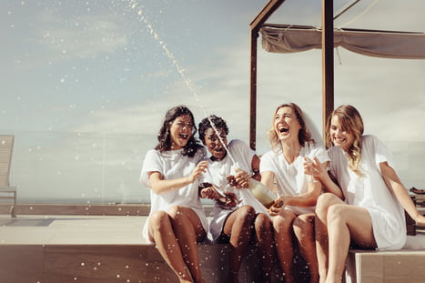 a group of friends popping a bottle of champagne by a pool 